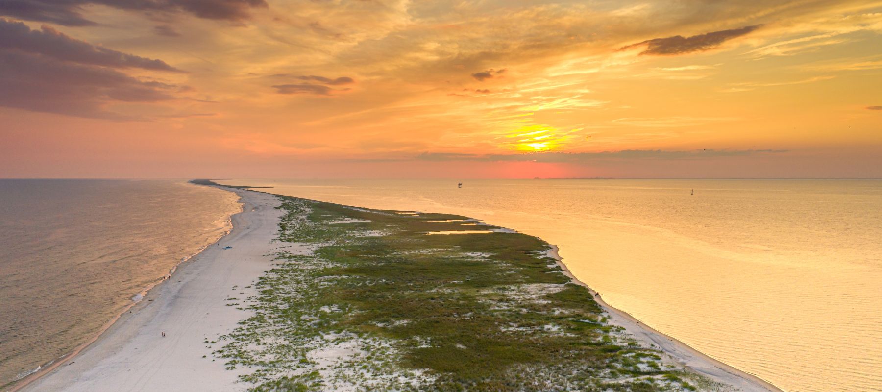 Aerial view of Dauphin Island, Alabama at sunset with golden light reflecting on calm ocean waters and the shoreline